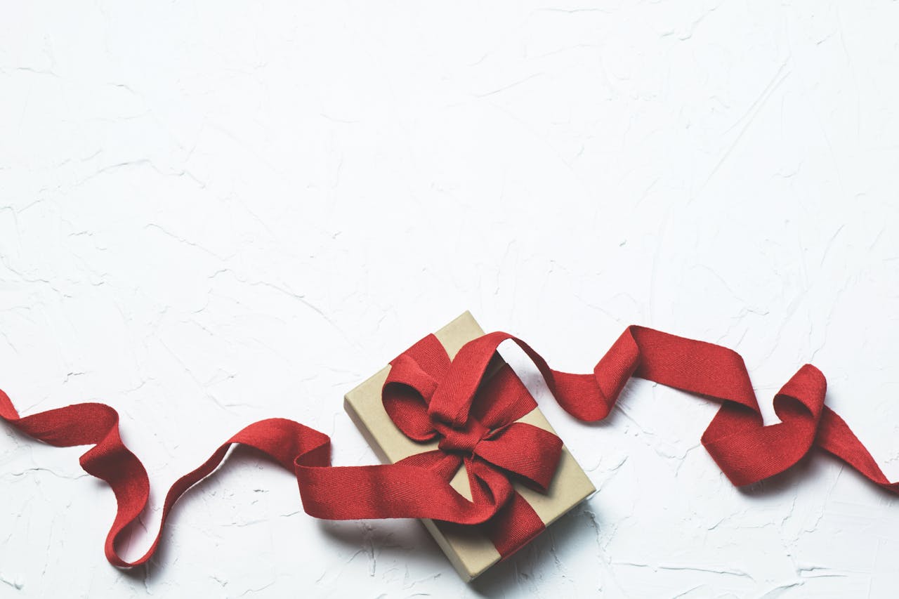 An elegant gift box with a flowing red ribbon on a textured white background, perfect for celebrations.
